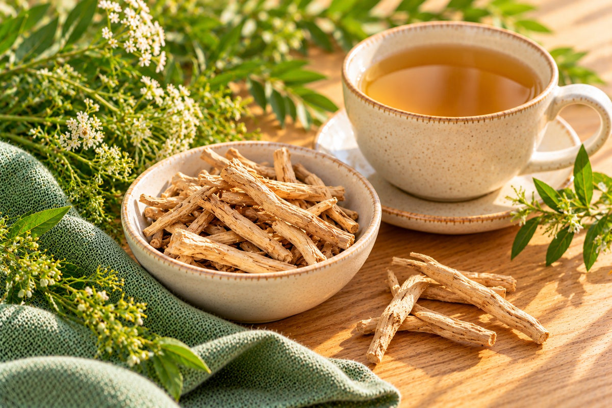 Dried shatavari root pieces in a small bowl beside a cup of herbal tea and a sprig of greenery
